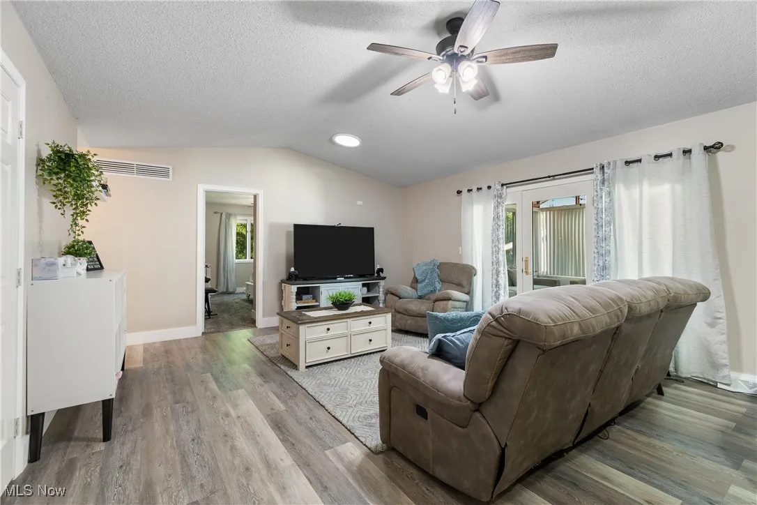 Living room featuring vaulted ceiling, a ceiling fan, wood finished floors, and a textured ceiling