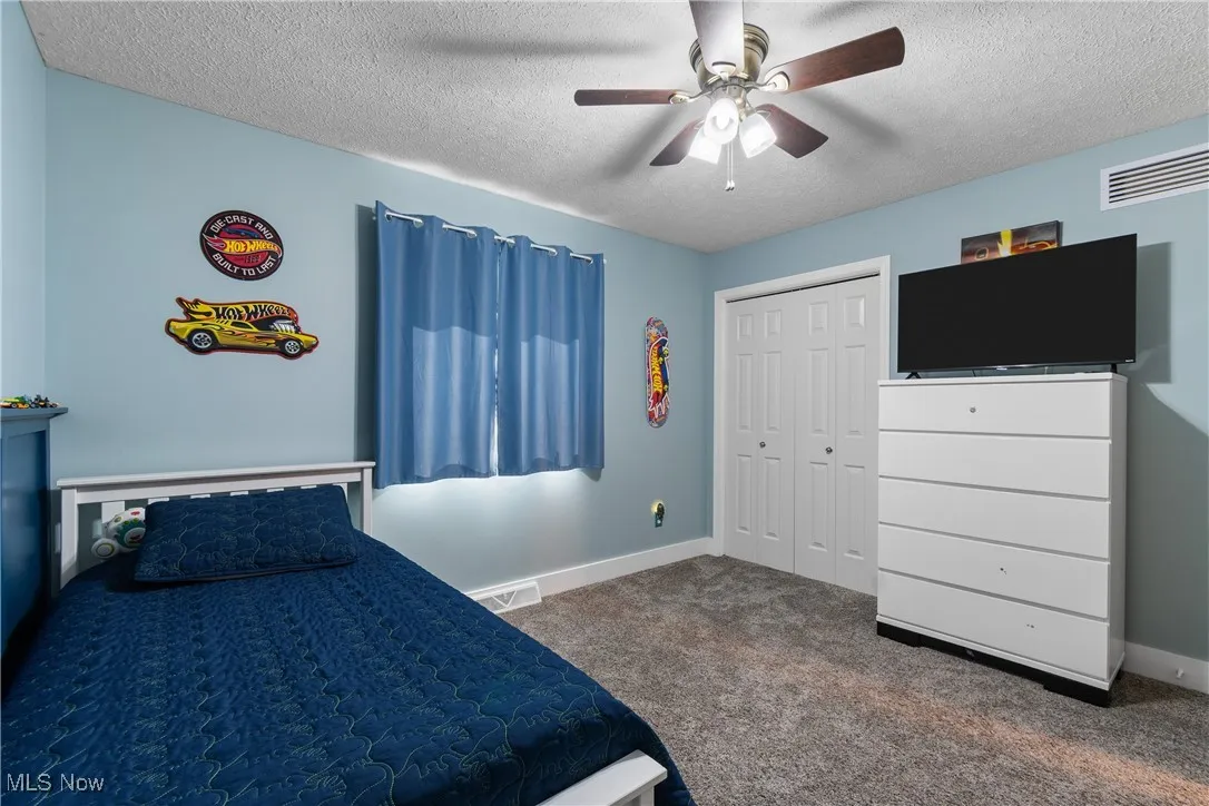 Bedroom with dark colored carpet, a textured ceiling, a closet, and ceiling fan
