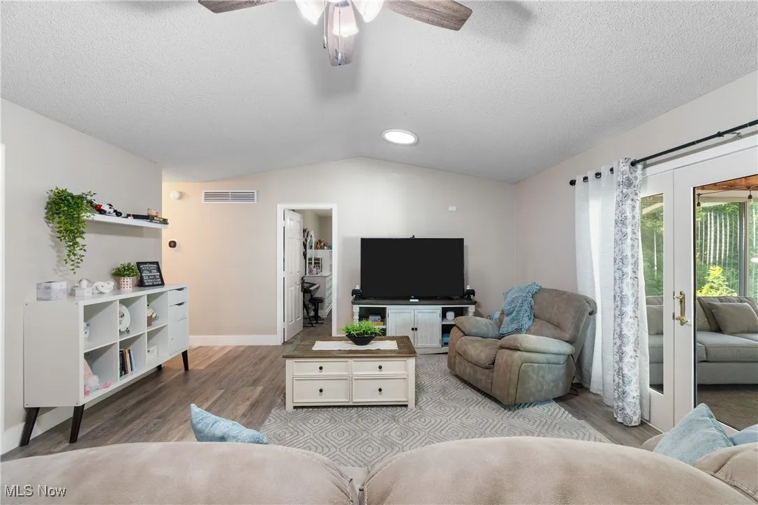 Living area with wood finished floors, vaulted ceiling, a ceiling fan, a textured ceiling, and french doors