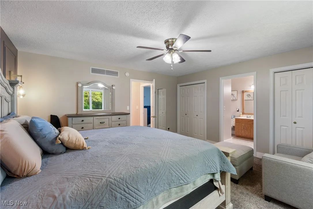 Carpeted bedroom with ensuite bath, multiple closets, ceiling fan, and a textured ceiling