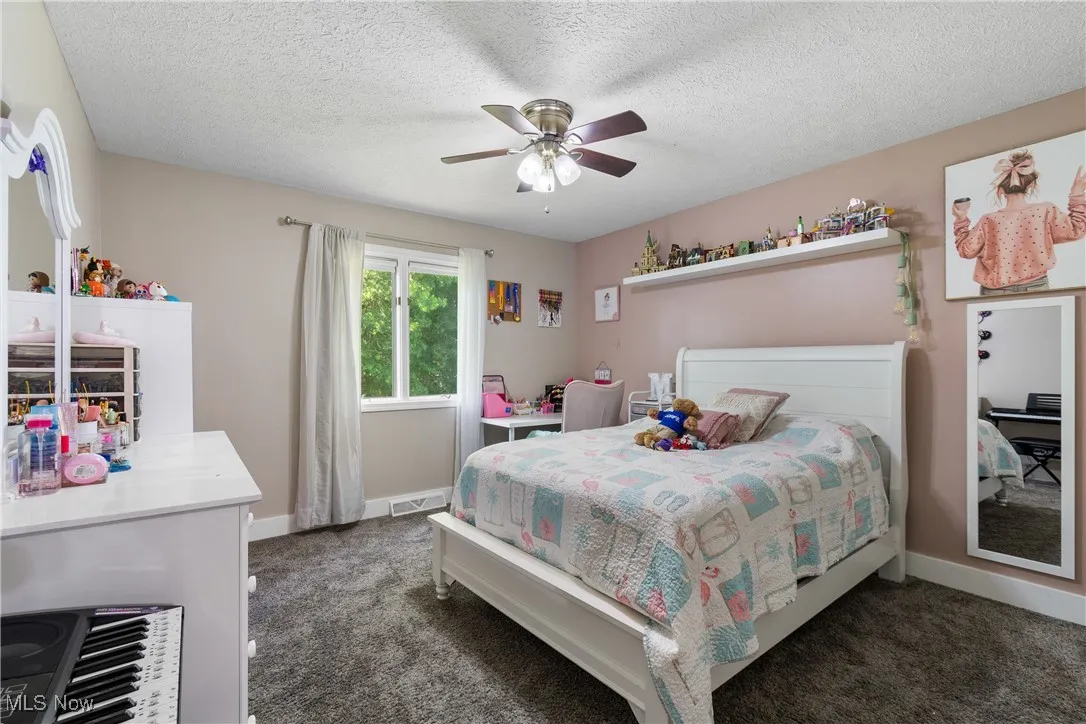 Carpeted bedroom with a ceiling fan and a textured ceiling