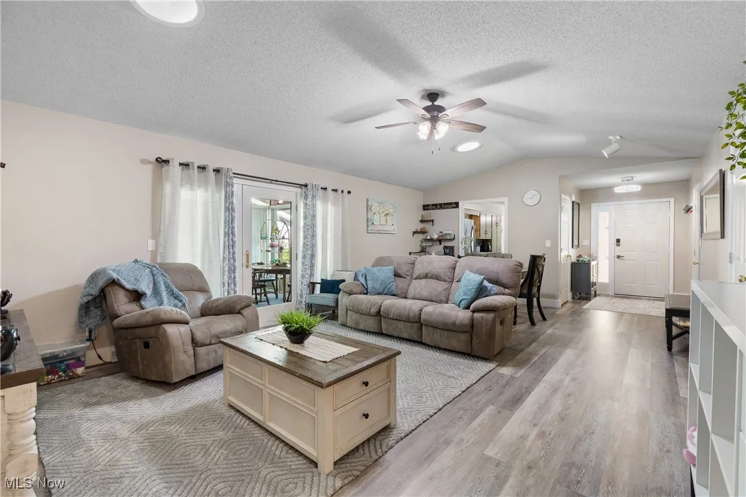Living room with a ceiling fan, vaulted ceiling, light wood finished floors, and a textured ceiling