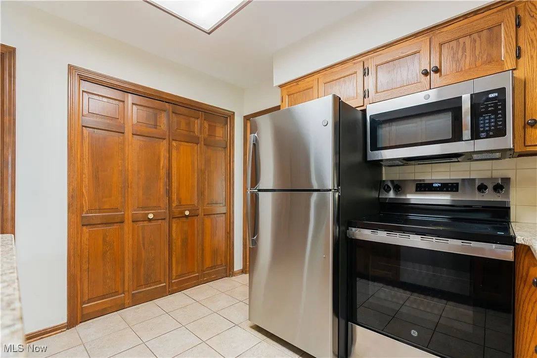 Kitchen featuring newer appliances with stainless steel finishes, backsplash, light tile patterned floors, granite countertops.