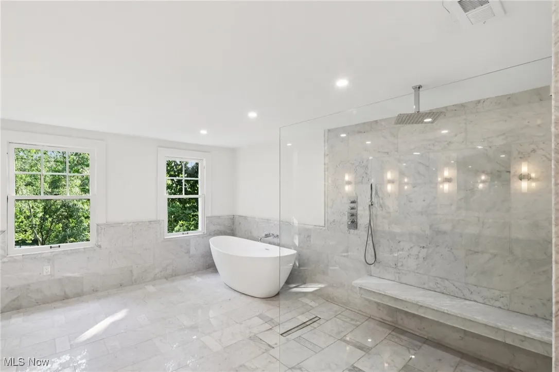 Bathroom featuring tile walls, a marble finish shower, a freestanding tub, marble tiled floors, and wainscoting