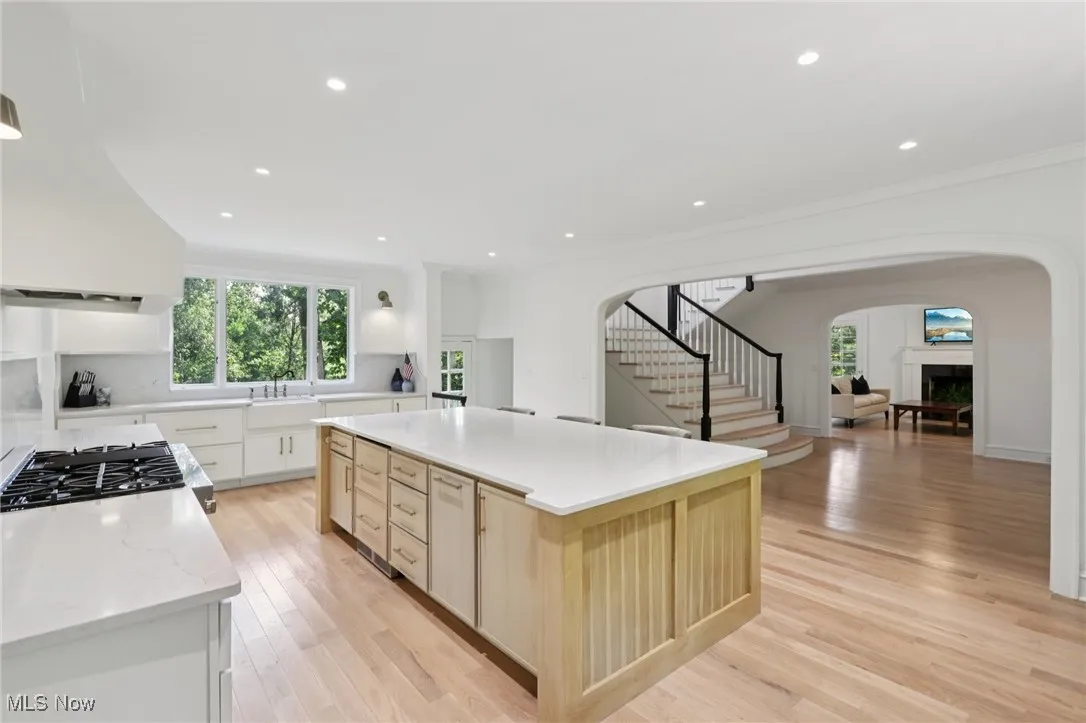 Kitchen with arched walkways, range hood, a large island, ornamental molding, and light wood finished floors