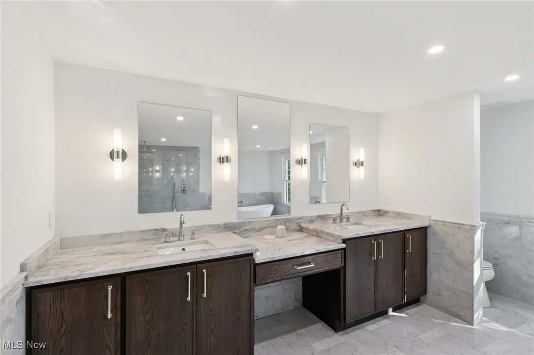 Bathroom featuring double vanity, tile walls, a walk in shower, marble finish flooring, and a tub