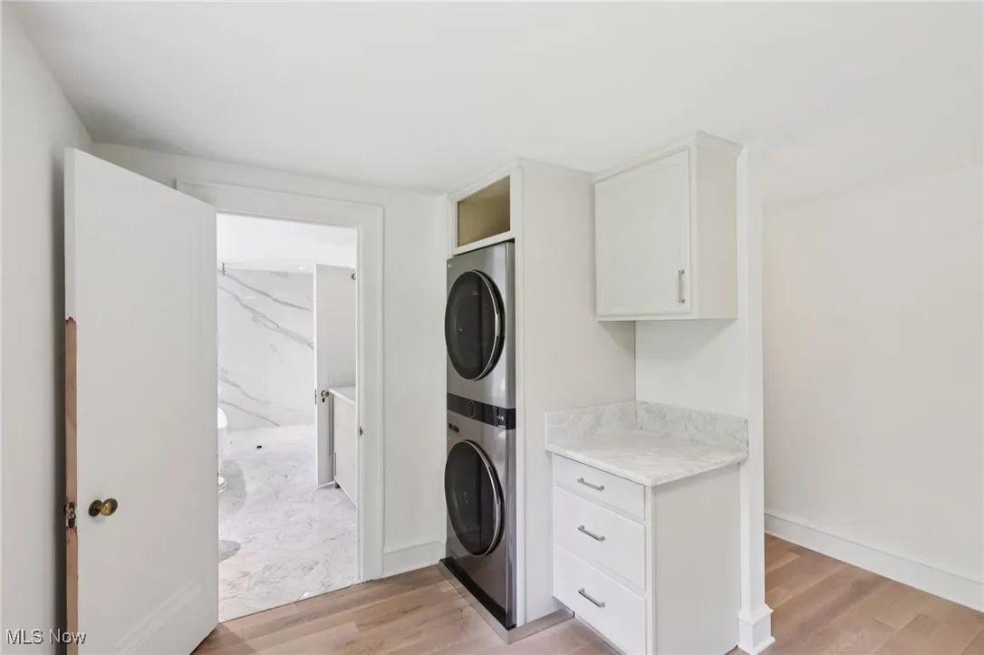 Laundry room with stacked washer / drying machine and light wood-type flooring