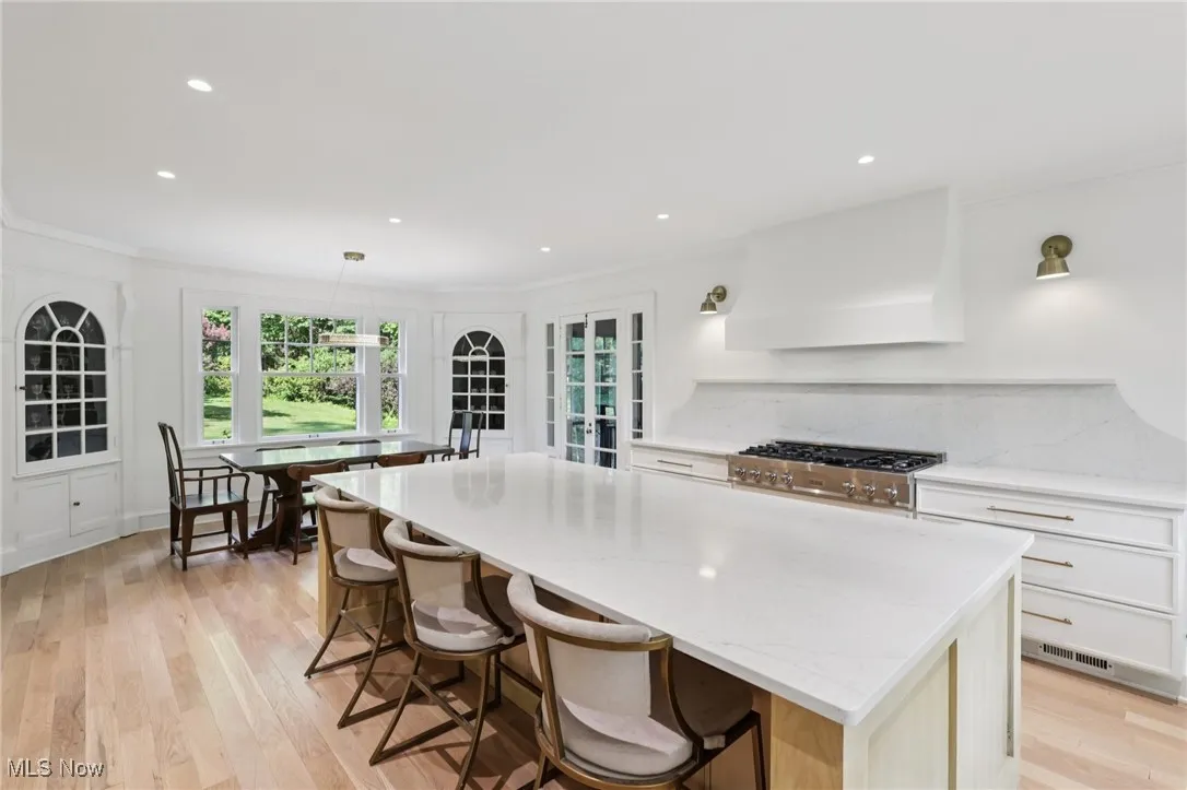 Kitchen with custom exhaust hood, crown molding, a kitchen island, light wood finished floors, and a kitchen breakfast bar