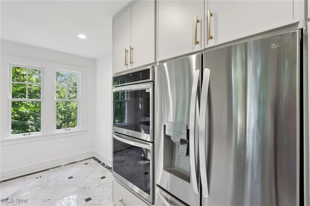 Kitchen featuring stainless steel appliances, recessed lighting, inlaid floor details, light marble finish flooring, and white cabinetry