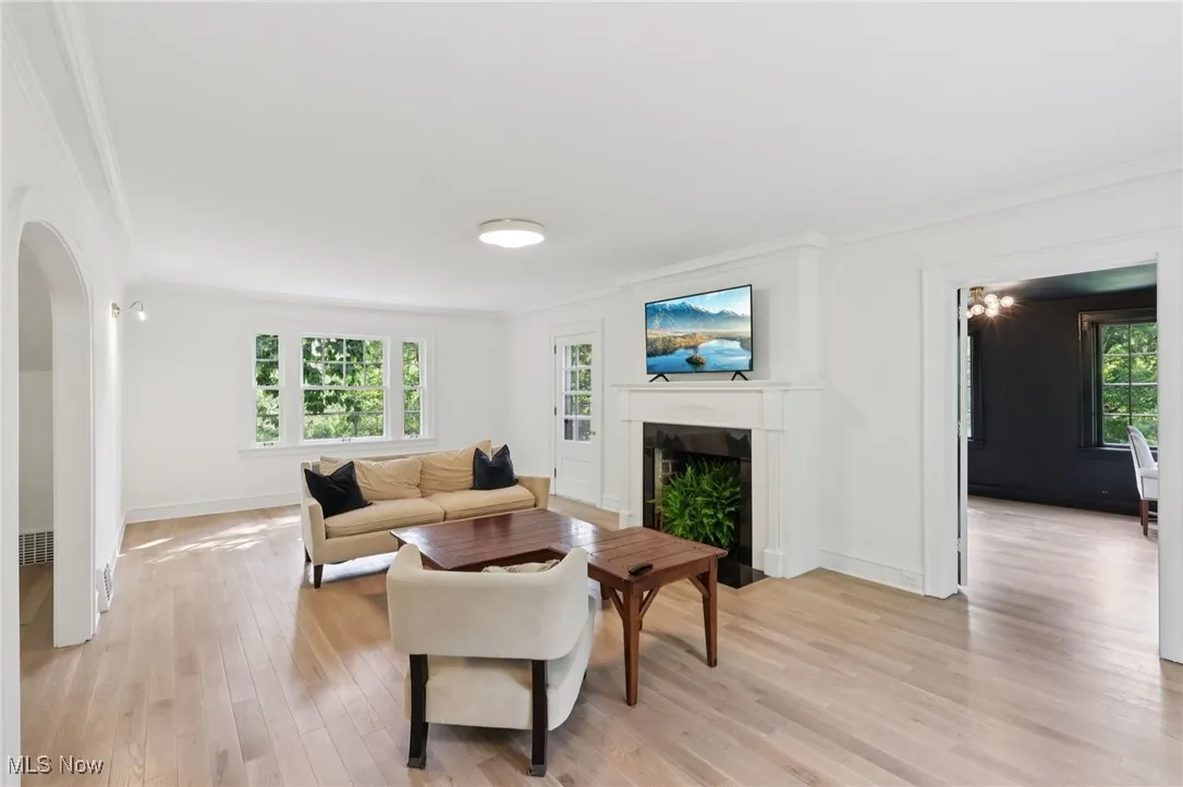 Living area featuring ornamental molding, a fireplace with flush hearth, arched walkways, and light wood finished floors