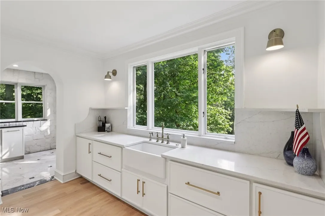 Kitchen featuring white cabinetry, ornamental molding, backsplash, light wood-type flooring, and light stone countertops