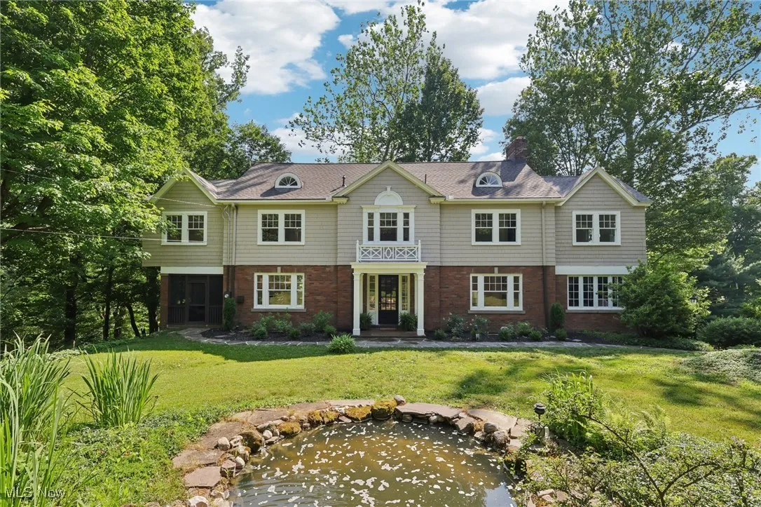 View of front of house featuring brick siding, a front yard, a small pond, and a chimney