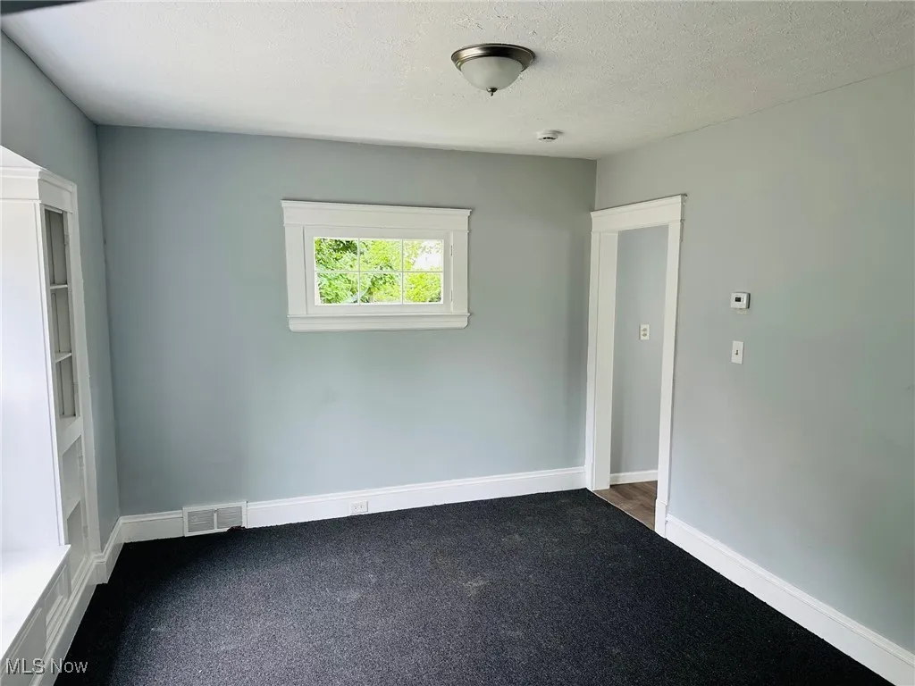 Empty room featuring dark carpet, a smoke detector, and a textured ceiling