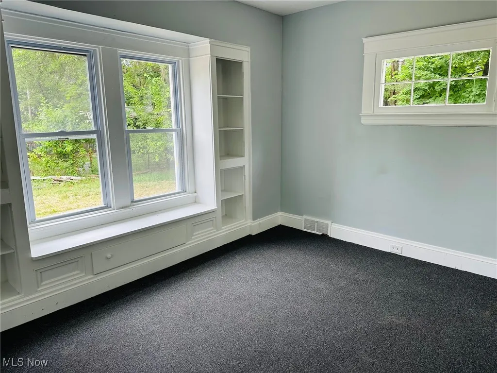 Empty room featuring healthy amount of natural light and dark colored carpet