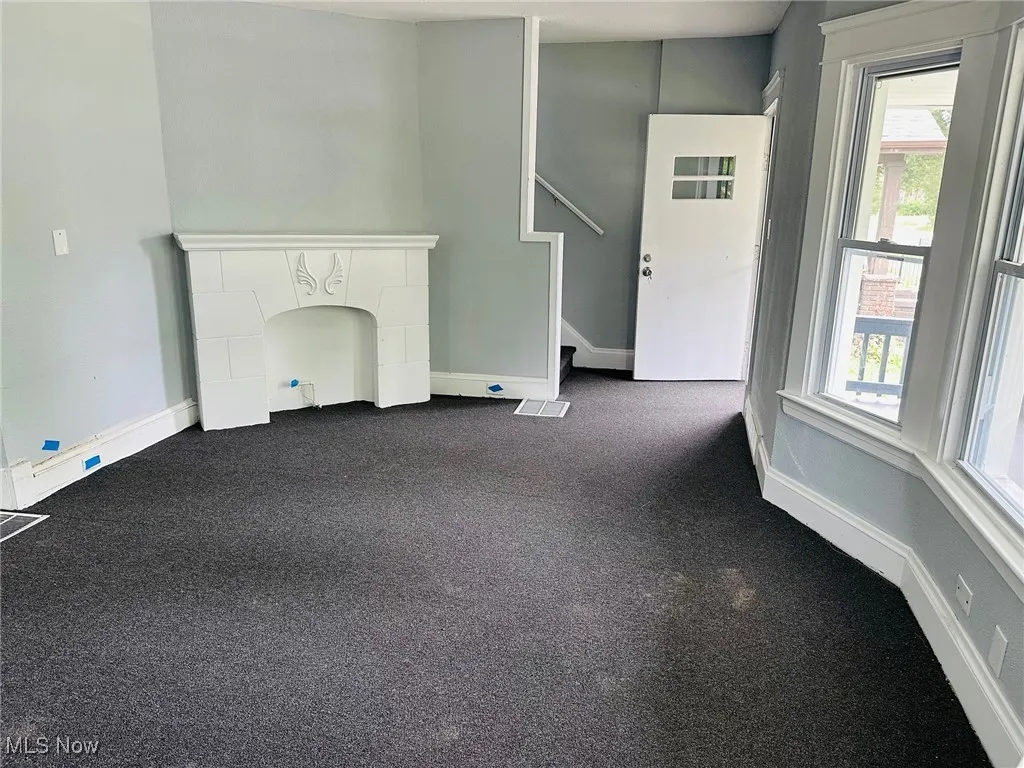 Unfurnished living room with plenty of natural light, stairway, and dark colored carpet