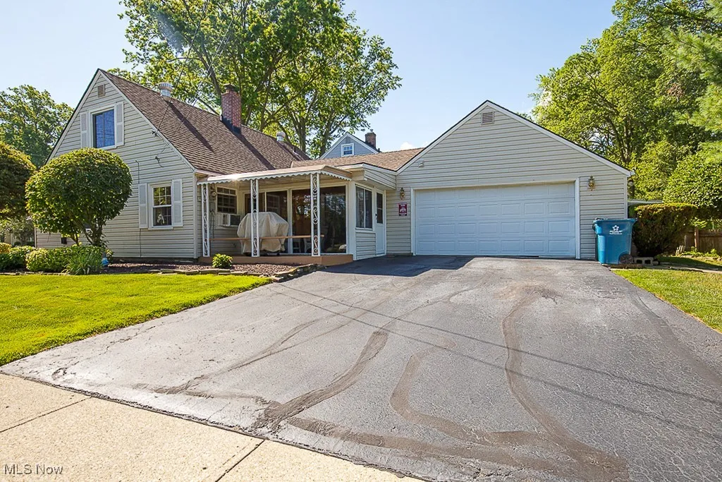 View of front of home featuring driveway, a front yard, an attached garage, a chimney, and covered porch