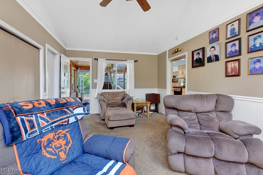Carpeted living area with wainscoting, ceiling fan, and crown molding