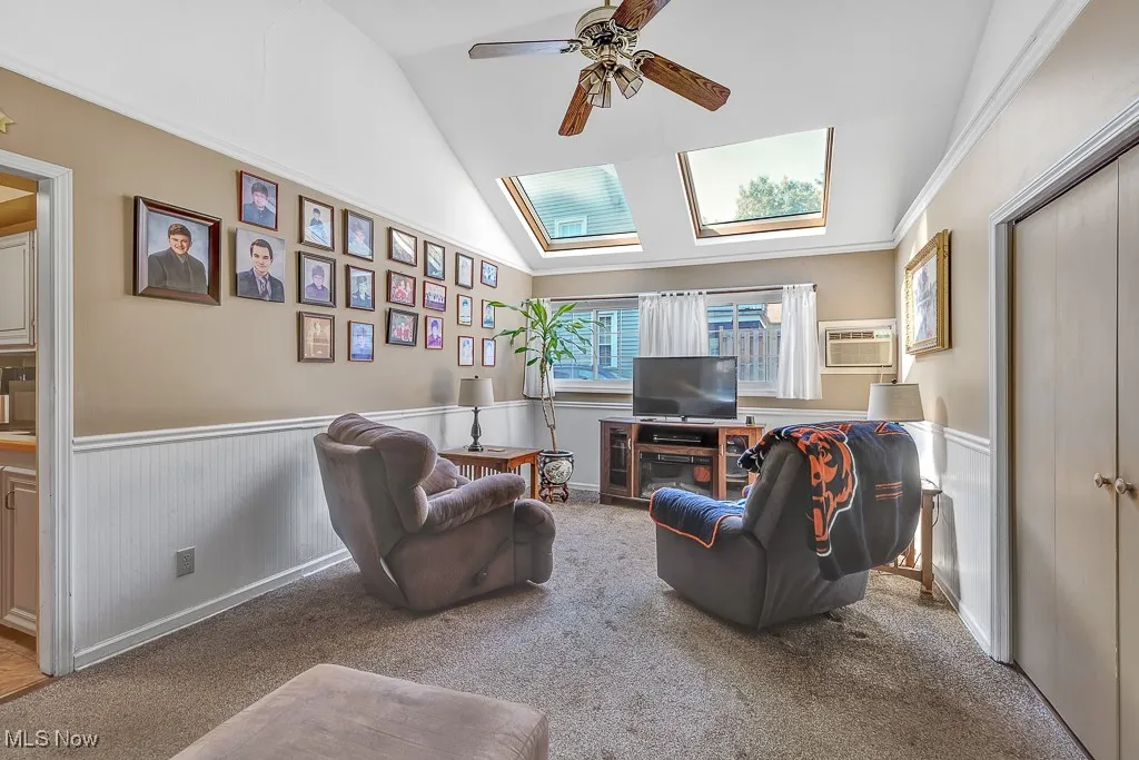 Living area featuring lofted ceiling, wainscoting, a wall mounted AC, ceiling fan, and carpet