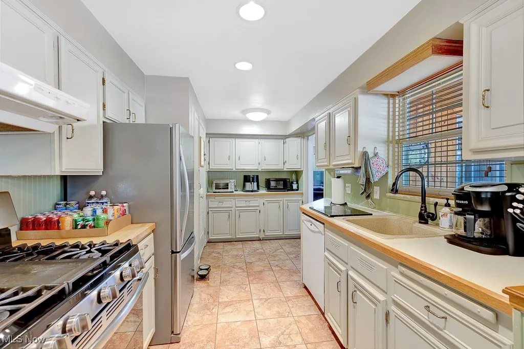 Kitchen featuring stainless steel gas range oven, dishwasher, light countertops, white cabinets, and ventilation hood