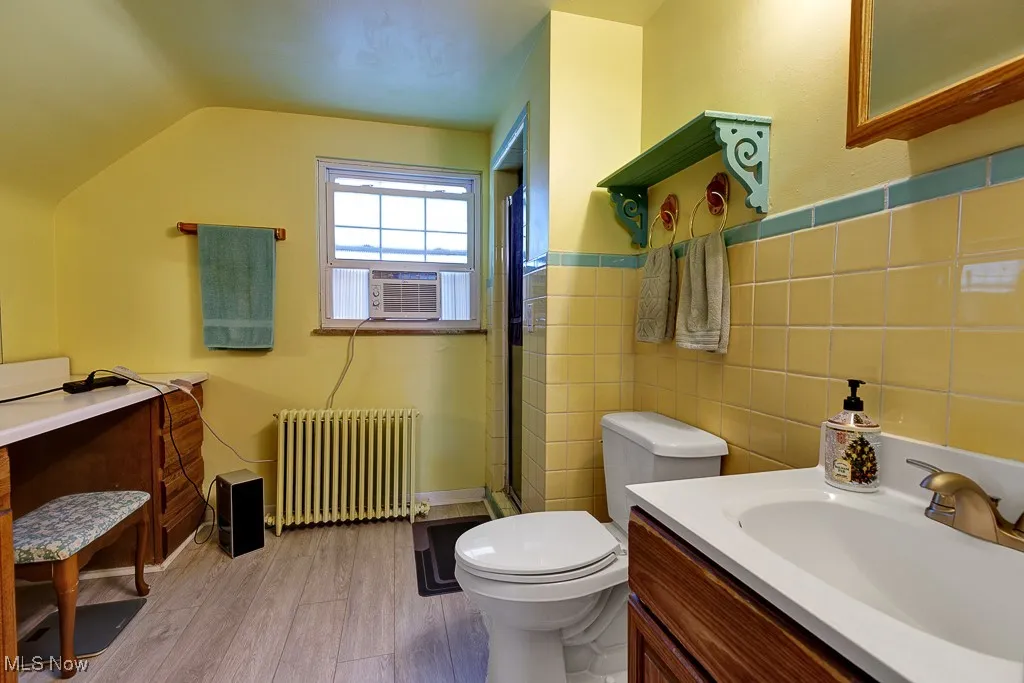 Bathroom featuring radiator, walk in shower, vanity, wood finished floors, and vaulted ceiling