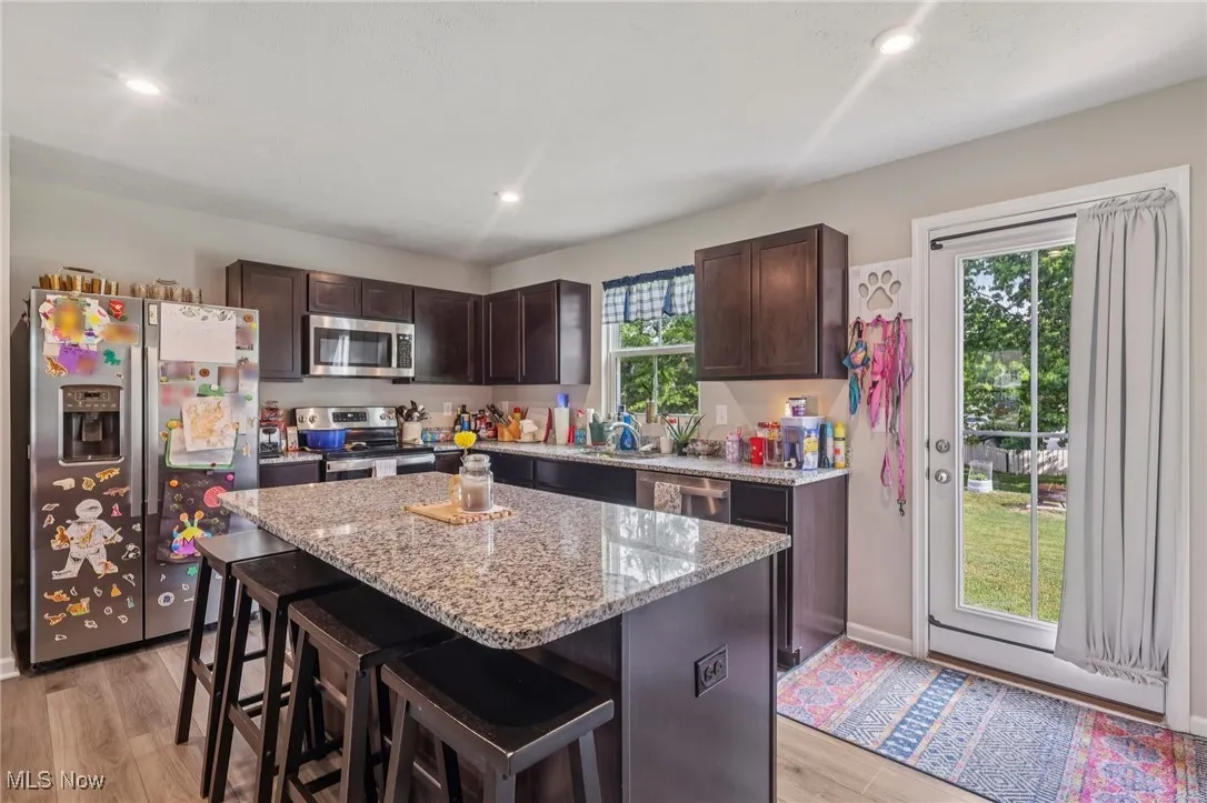 Kitchen with stainless steel appliances, dark brown cabinets, a breakfast bar area, light stone countertops, and recessed lighting