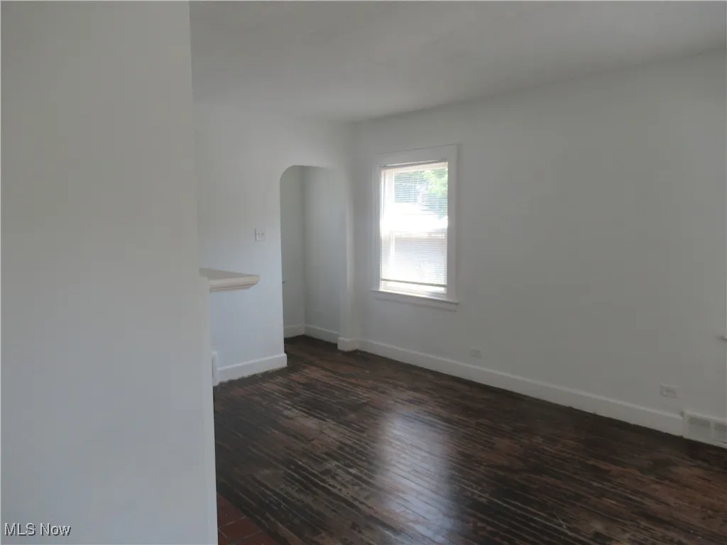 Spare room featuring arched walkways and dark wood-style floors