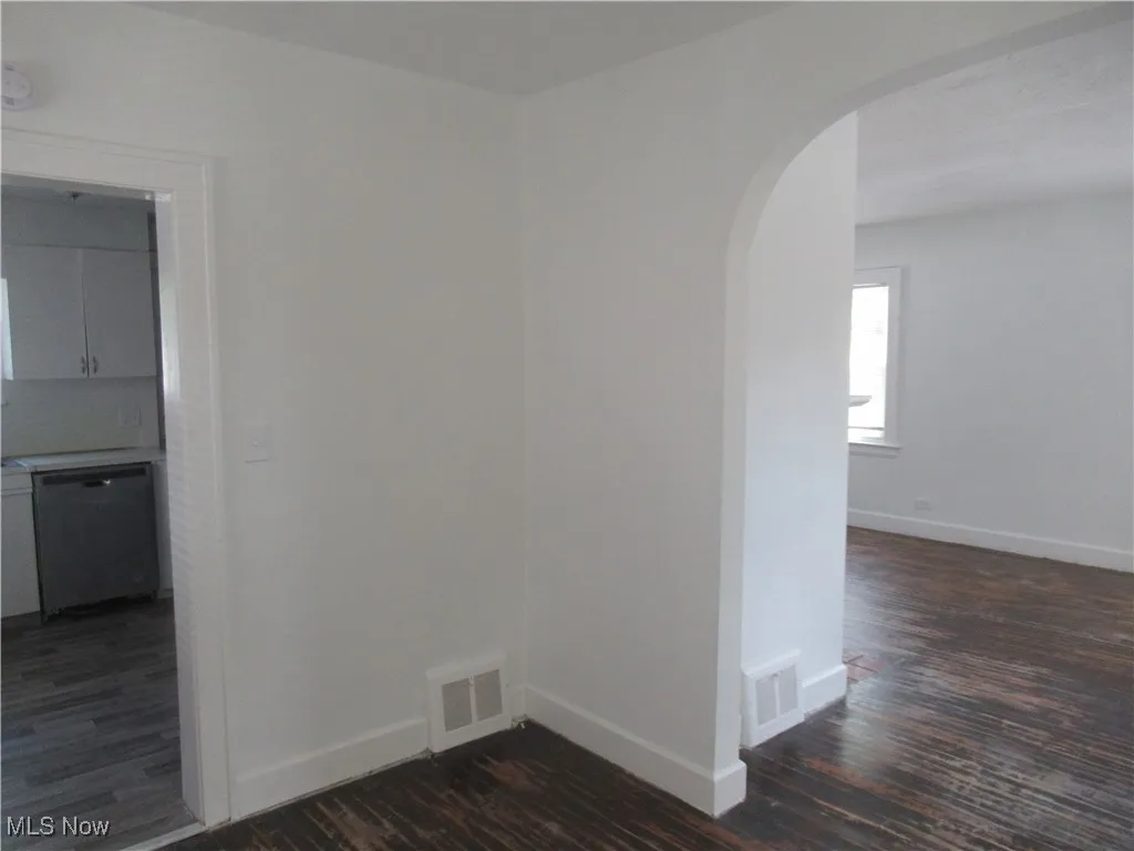 Unfurnished room with arched walkways and dark wood-style flooring