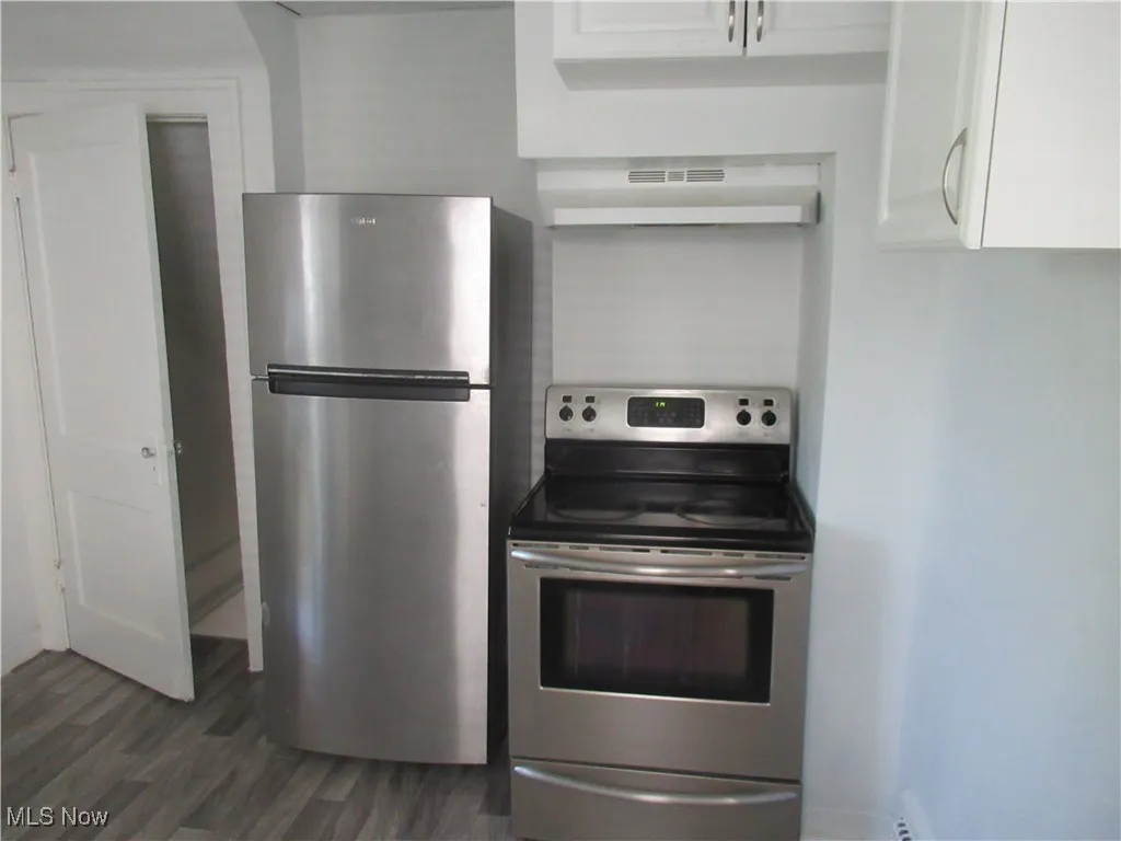 Kitchen featuring appliances with stainless steel finishes, under cabinet range hood, wood finished floors, and white cabinetry