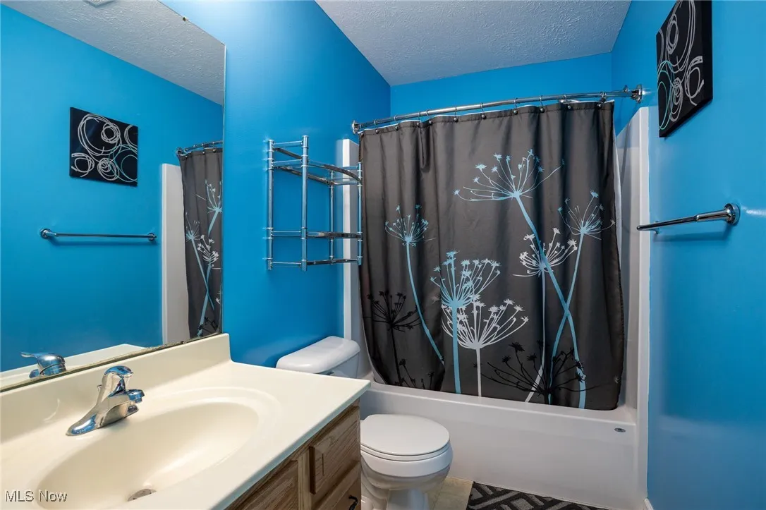 Full bath featuring a textured ceiling, vanity, and shower / tub combo with curtain