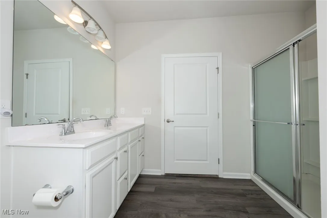 Full bath with double vanity, wood finished floors, and an enclosed shower