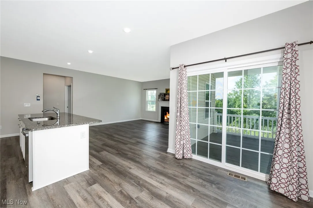 Kitchen featuring stone countertops, dark wood-style floors, a center island with sink, a lit fireplace, and open floor plan