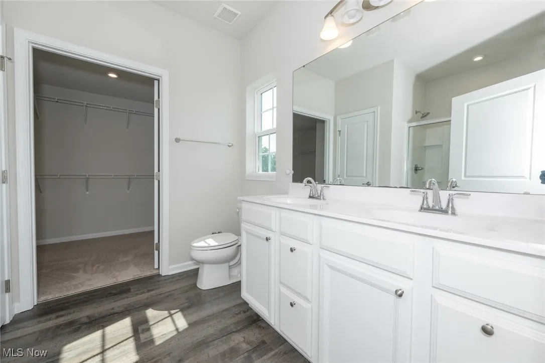 Full bathroom featuring wood finished floors, double vanity, a shower, and a spacious closet