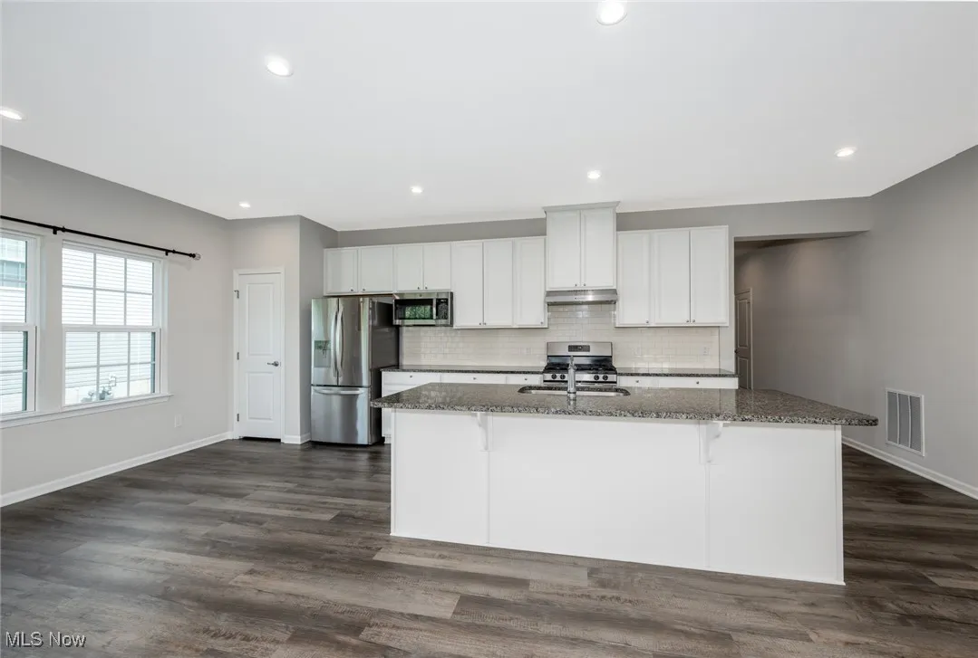 Kitchen with stainless steel appliances, dark stone countertops, an island with sink, a breakfast bar, and dark wood-type flooring