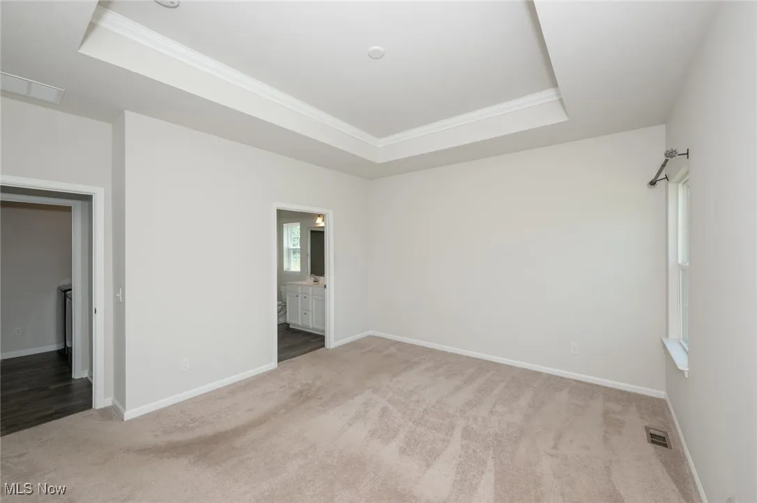 Unfurnished bedroom with a raised ceiling, light carpet, crown molding, and connected bathroom