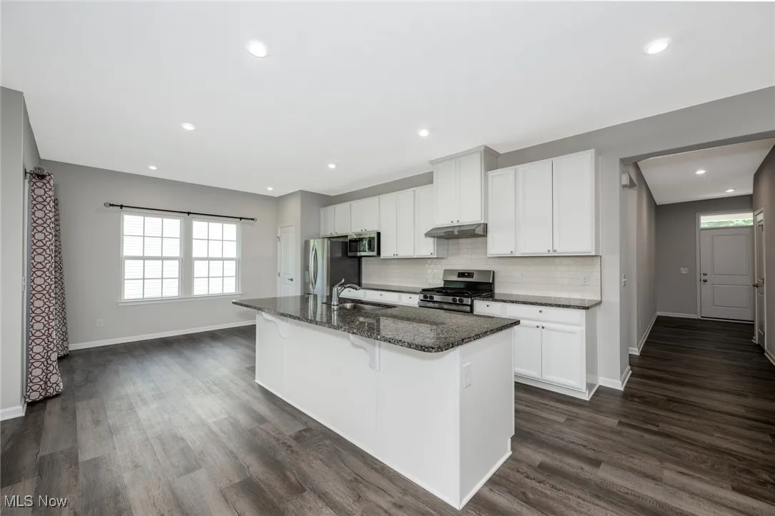 Kitchen featuring stainless steel appliances, a center island with sink, a kitchen bar, dark wood finished floors, and tasteful backsplash