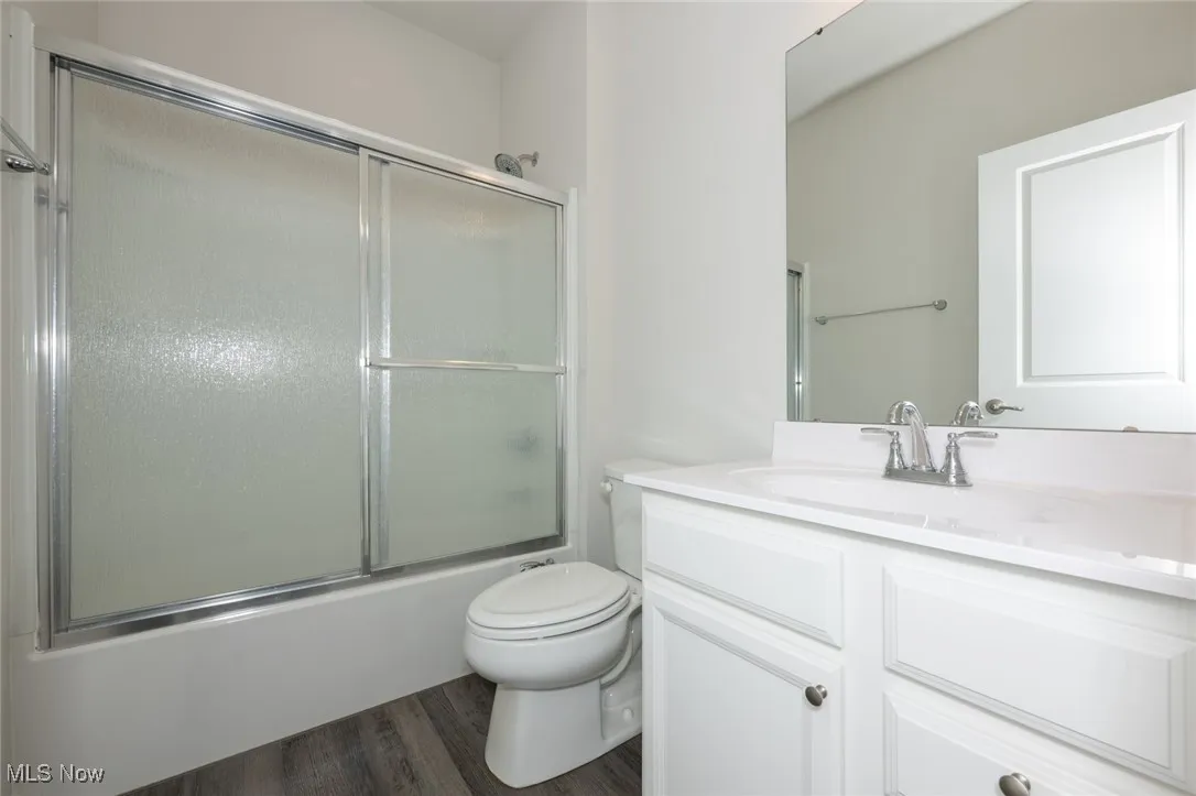 Bathroom featuring vanity, enclosed tub / shower combo, and wood finished floors