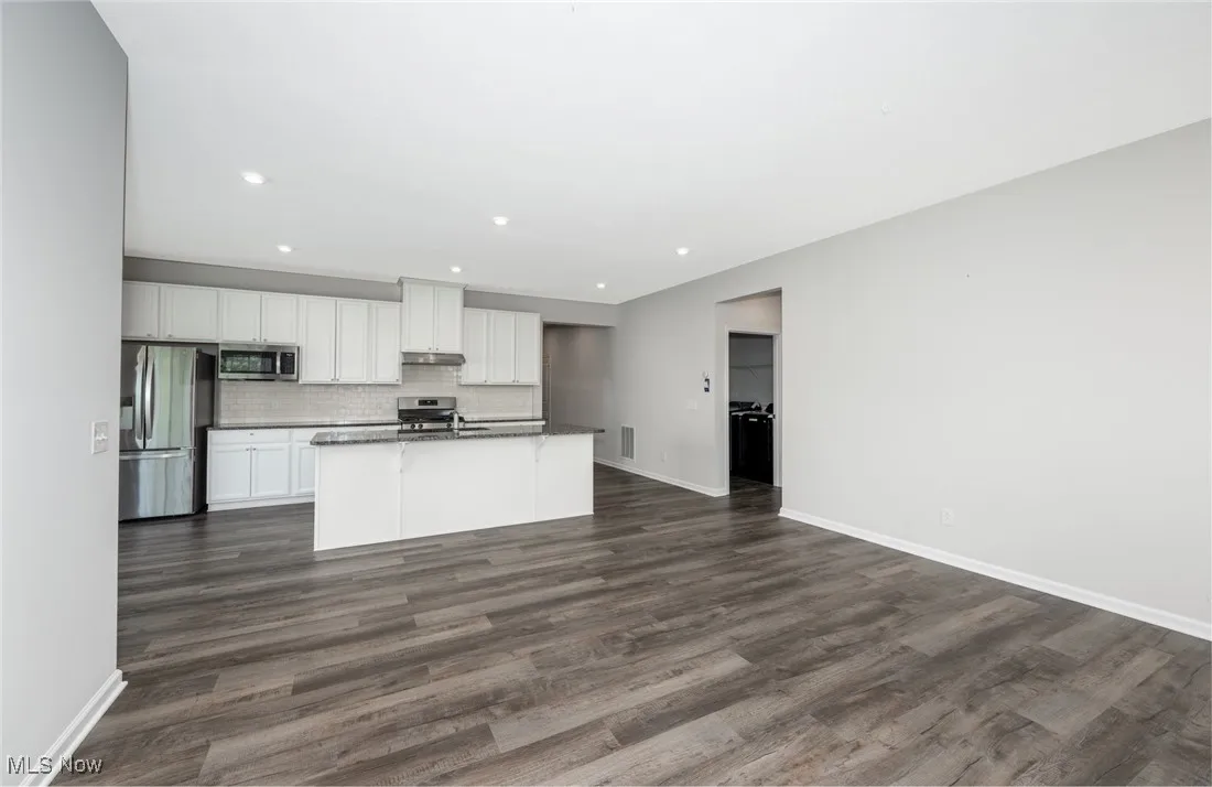Kitchen with stainless steel appliances, under cabinet range hood, white cabinets, dark countertops, and a kitchen island with sink