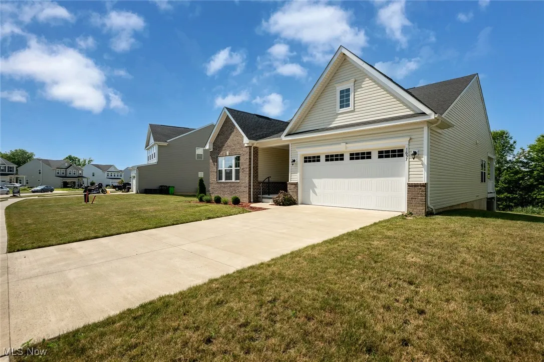 View of front facade featuring brick siding, concrete driveway, a front lawn, and an attached garage