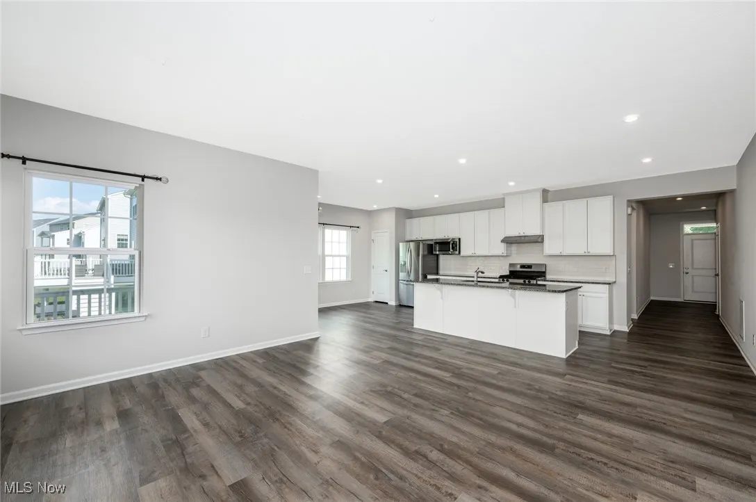 Kitchen featuring stainless steel appliances, open floor plan, an island with sink, white cabinets, and dark wood-type flooring