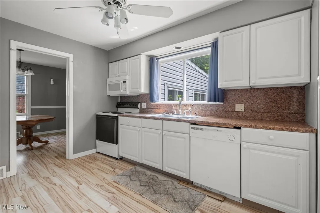 Kitchen featuring white appliances, decorative backsplash, dark countertops, white cabinets, and ceiling fan