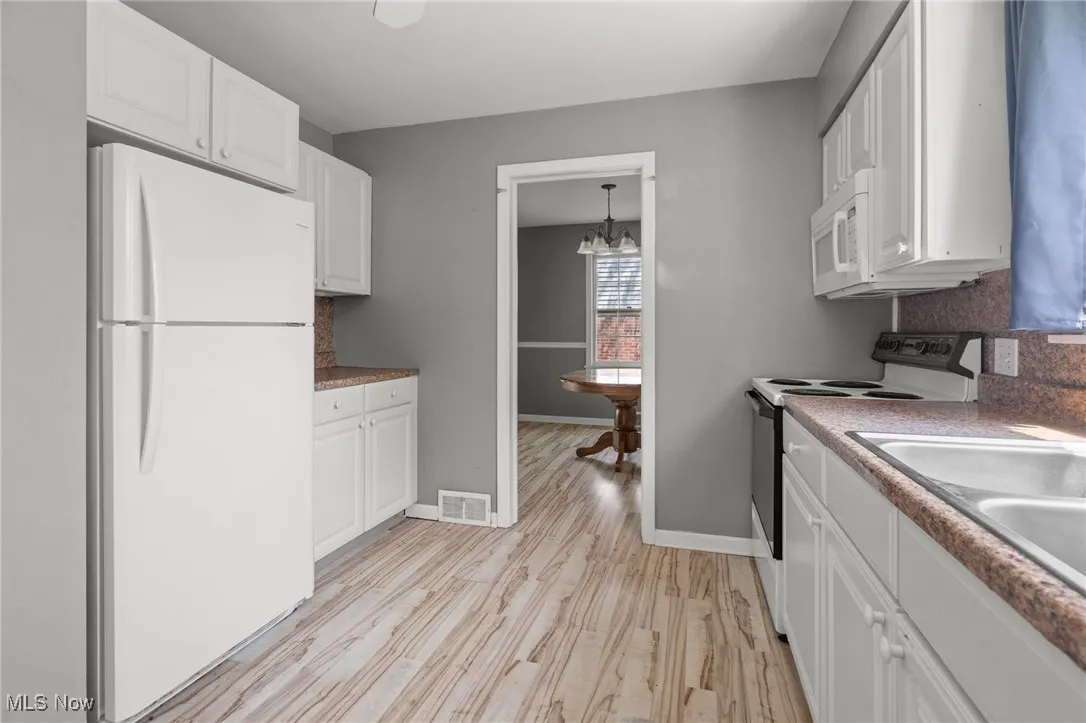 Kitchen with white appliances, white cabinetry, light wood-style flooring, a chandelier, and tasteful backsplash