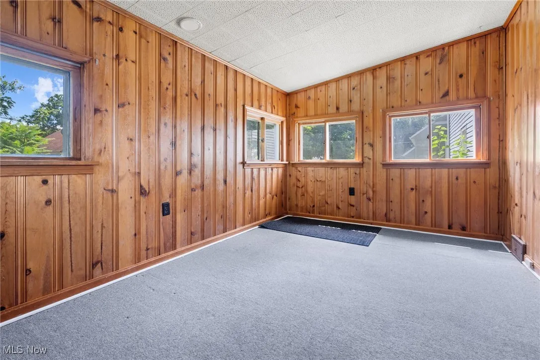 Carpeted empty room featuring wood walls and baseboards