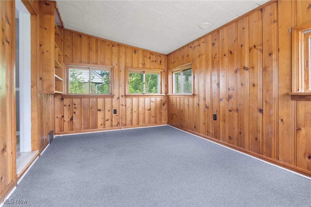Carpeted empty room featuring wood walls and vaulted ceiling