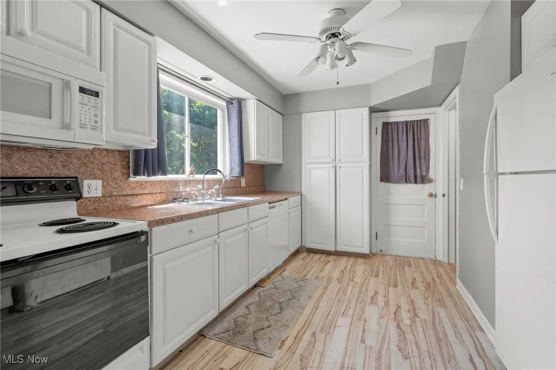 Kitchen featuring white appliances, white cabinetry, tasteful backsplash, a ceiling fan, and light wood-style flooring