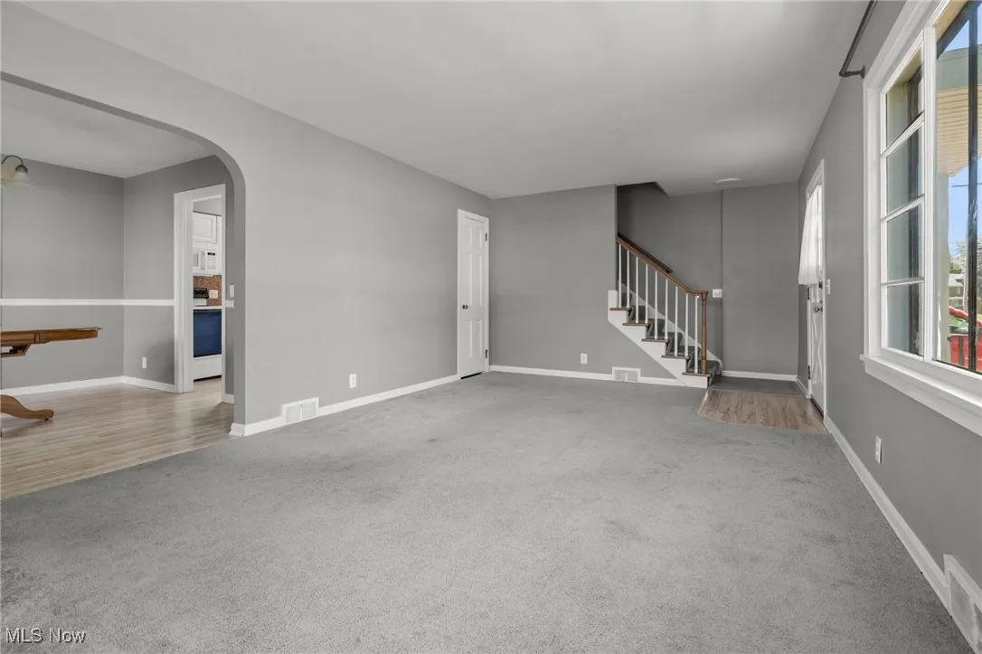 Unfurnished living room featuring carpet flooring, stairway, and arched walkways