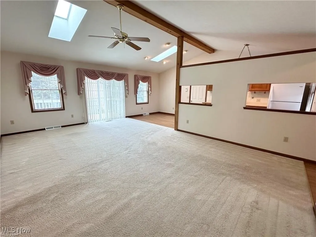 Great  room with a skylight, vaulted ceiling fan, and light colored carpet