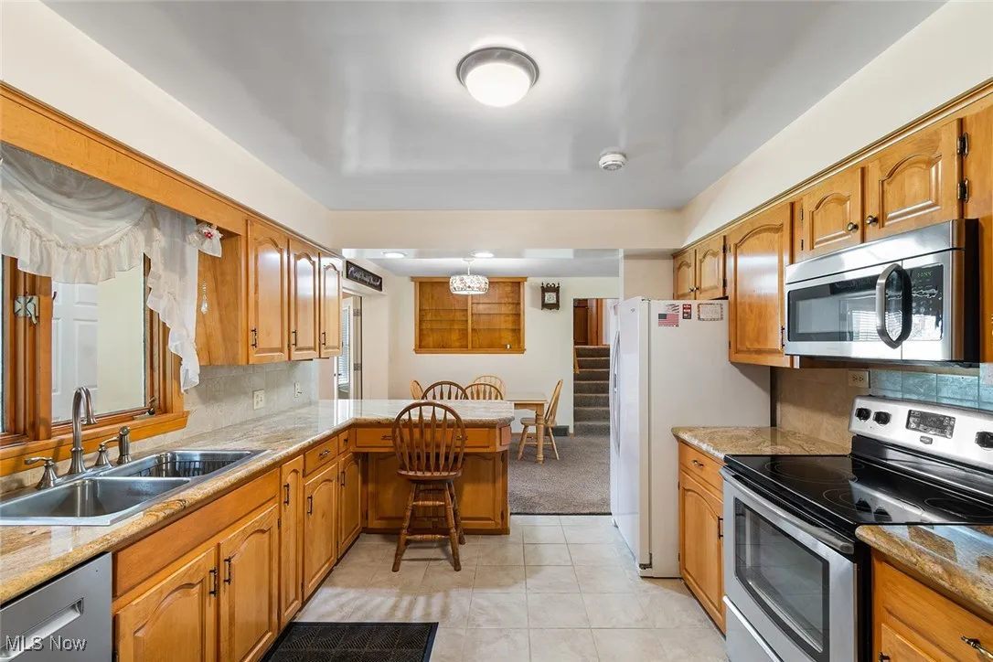 Kitchen with stainless steel appliances, a peninsula, tasteful backsplash, and brown cabinets