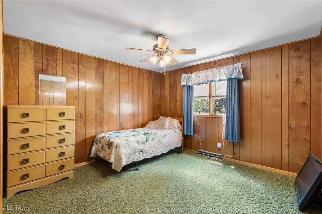 Carpeted bedroom featuring wooden walls and ceiling fan