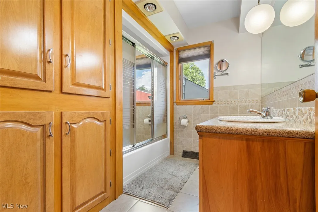 Bathroom featuring tile patterned flooring, vanity, shower / bath combination with glass door, and tile walls