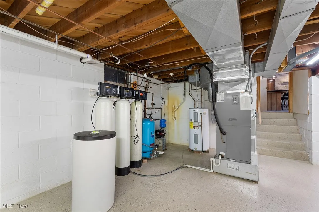 Unfinished basement featuring water heater, a water pressure tank, a water softener, and stairway